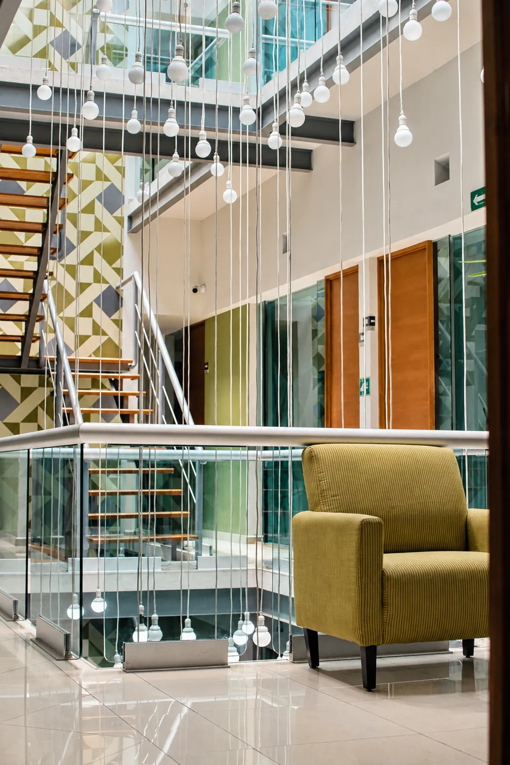 Atrio con luces colgantes, escalera y sillón verde oliva, OfiRent Condesa, Ciudad de México