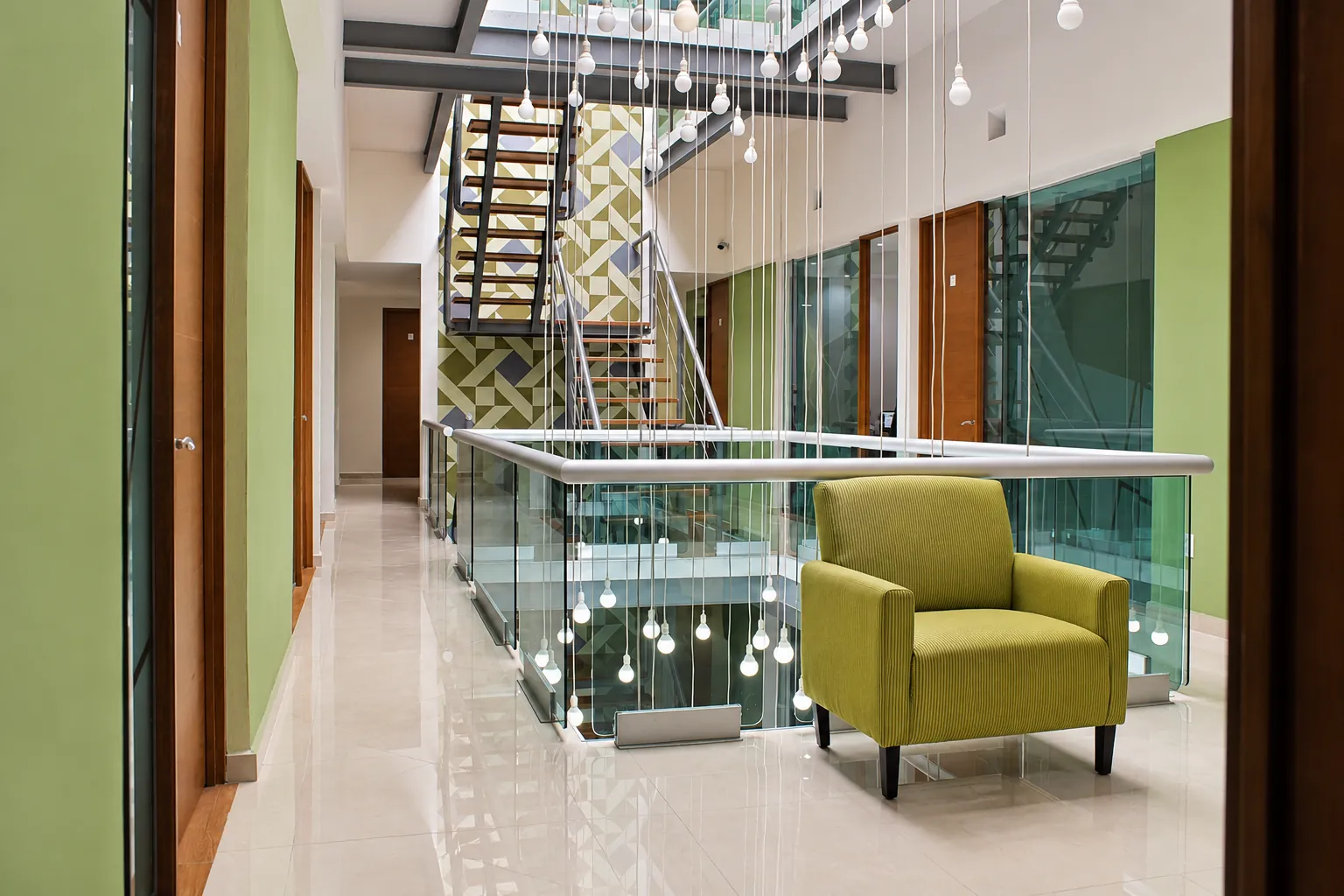 Atrio con escalera, barandal de cristal y sillón verde oliva, OfiRent Condesa, Ciudad de México