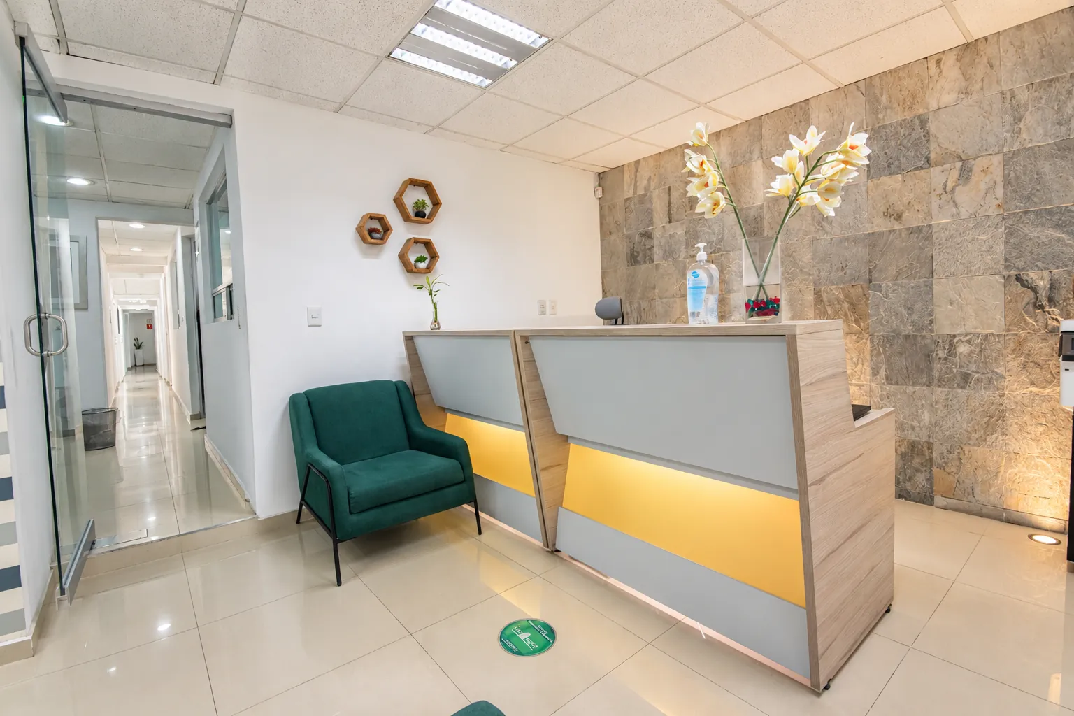 Recepción con sillones verdes, muro de piedra y pasillo con puertas de cristal, OfiRent Del Valle, Ciudad de México
