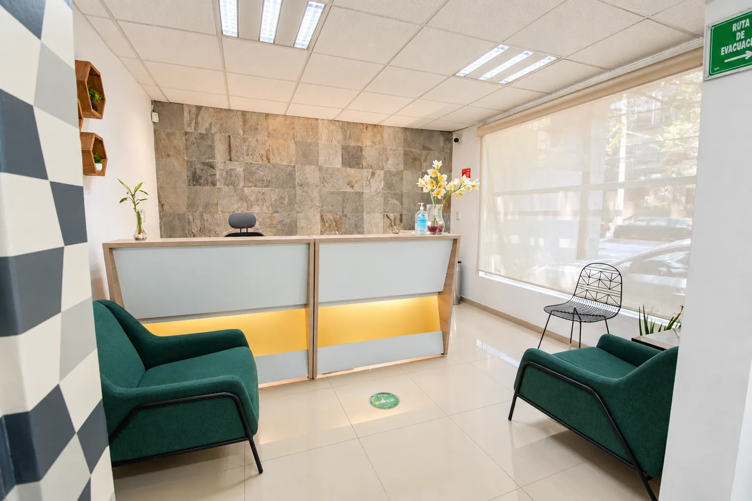Recepción con mostrador iluminado, sillones verdes y muro de piedra, OfiRent Del Valle, Ciudad de México