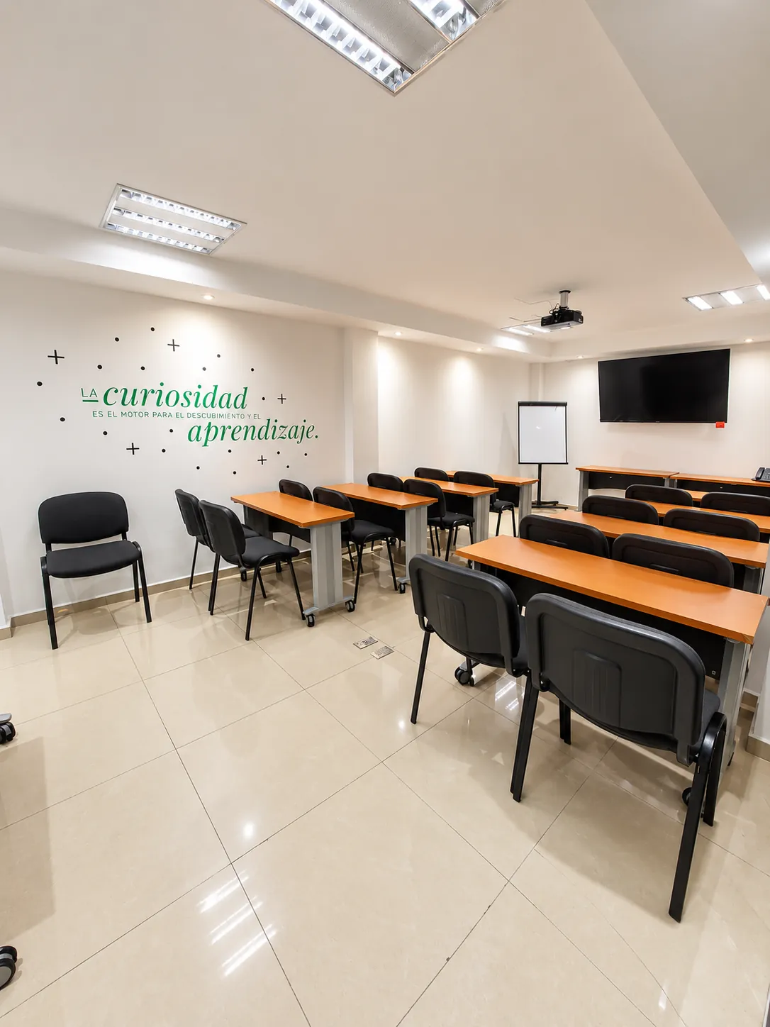 Sala de capacitación con filas de escritorios y sillas, pantalla y un mensaje en la pared, OfiRent Narvarte, Ciudad de México