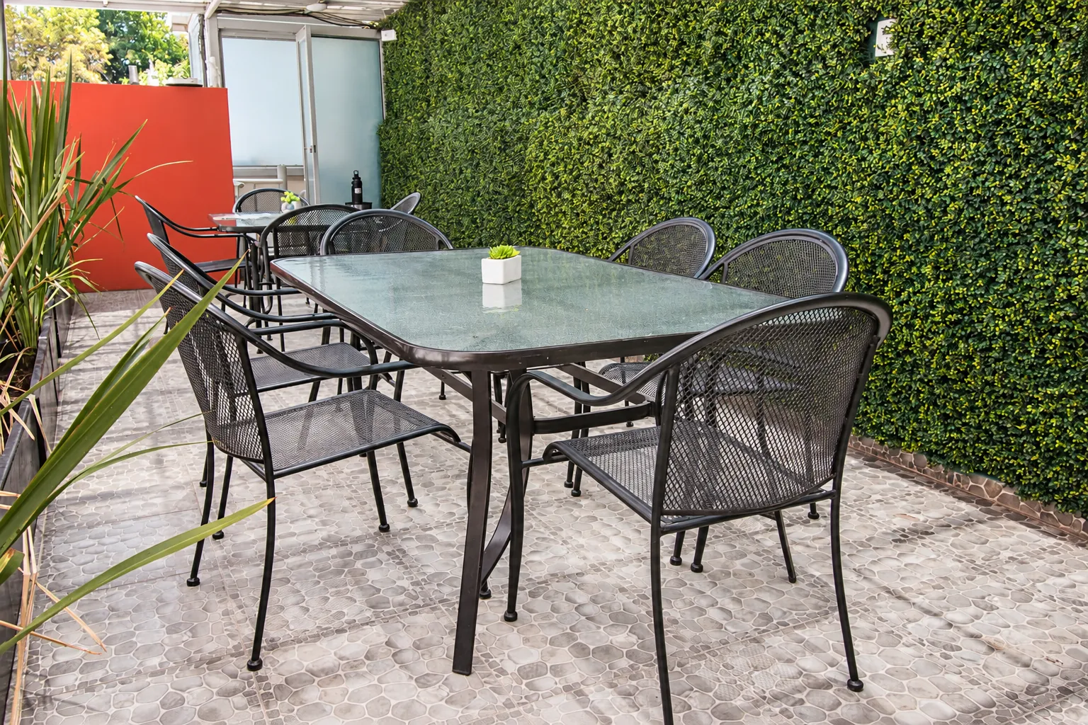 Patio con mesa de cristal, sillas y muro de plantas, OfiRent Narvarte, Ciudad de México