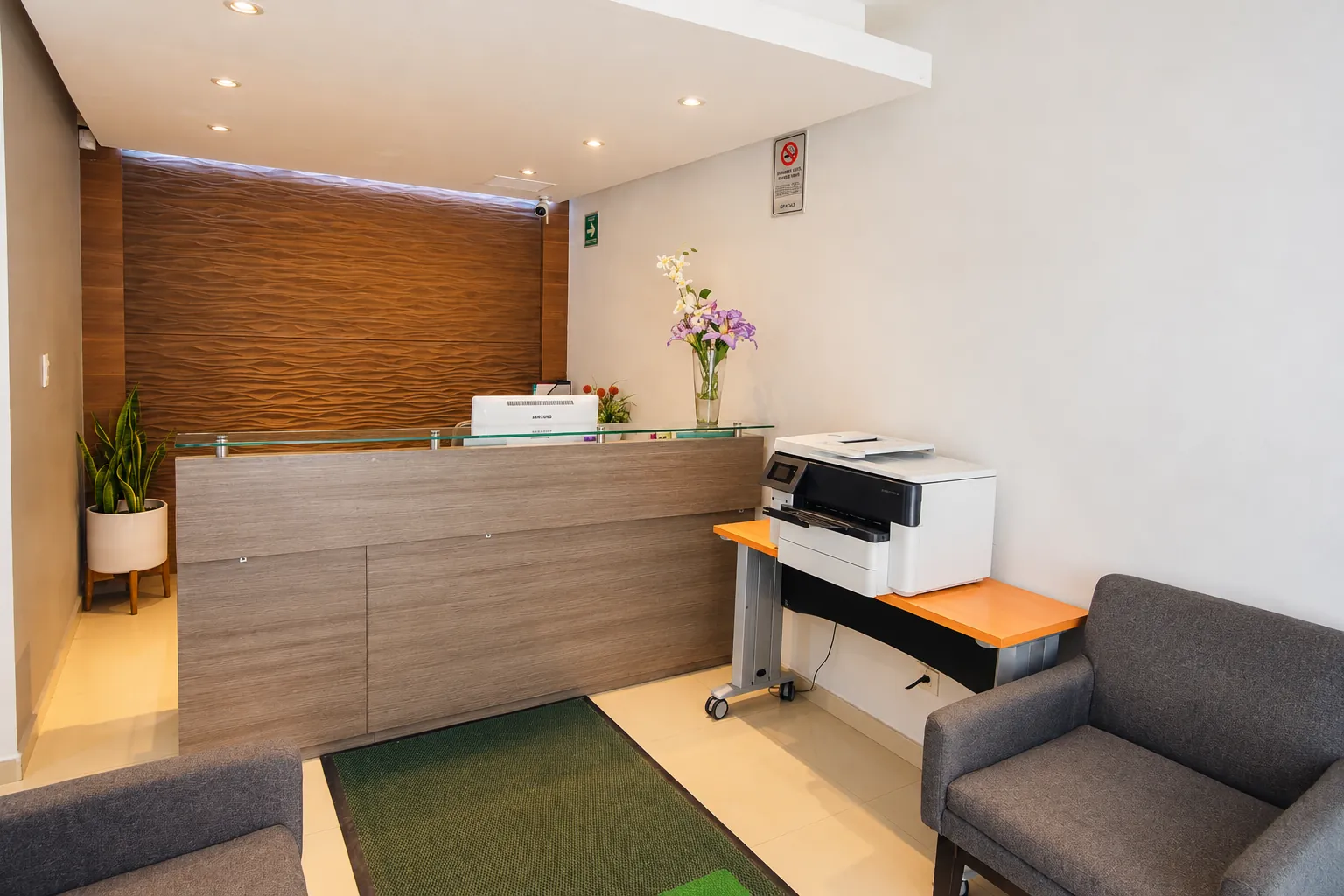 Recepción con mostrador de madera, sillones grises, flores y plantas, OfiRent Narvarte, Ciudad de México
