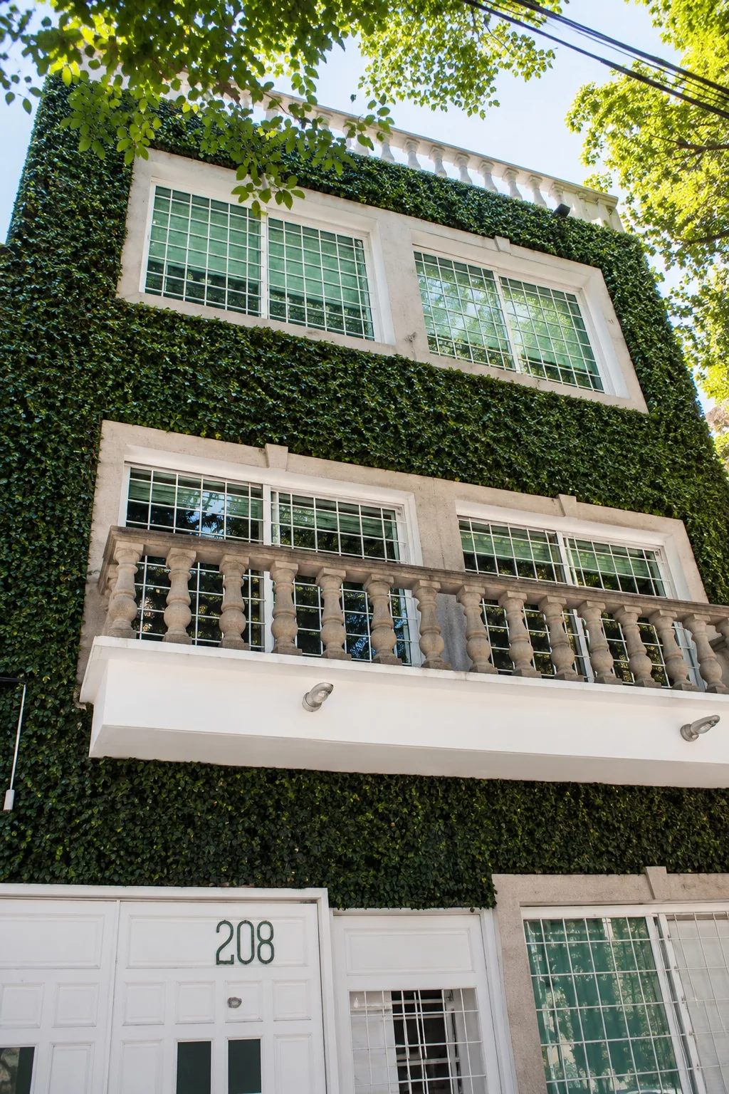 Fachada cubierta de plantas con balcón y el número 208, OfiRent Roma, Ciudad de México