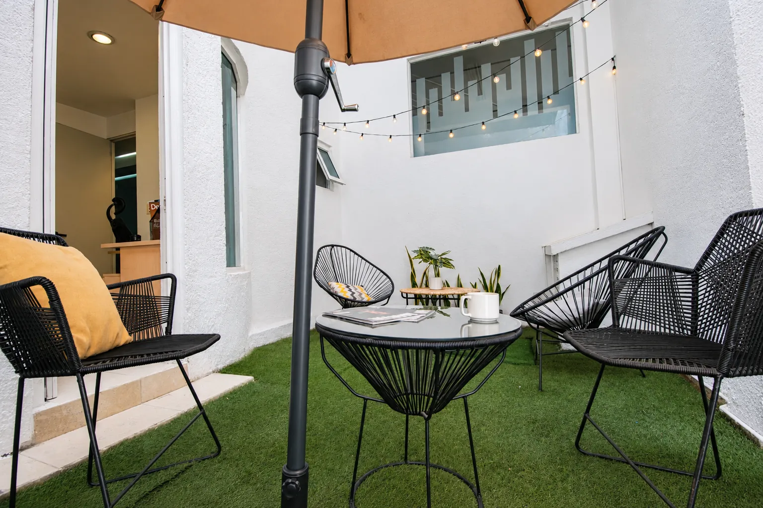 Patio con sillones de alambre, césped artificial y luces cálidas, OfiRent Roma, Ciudad de México