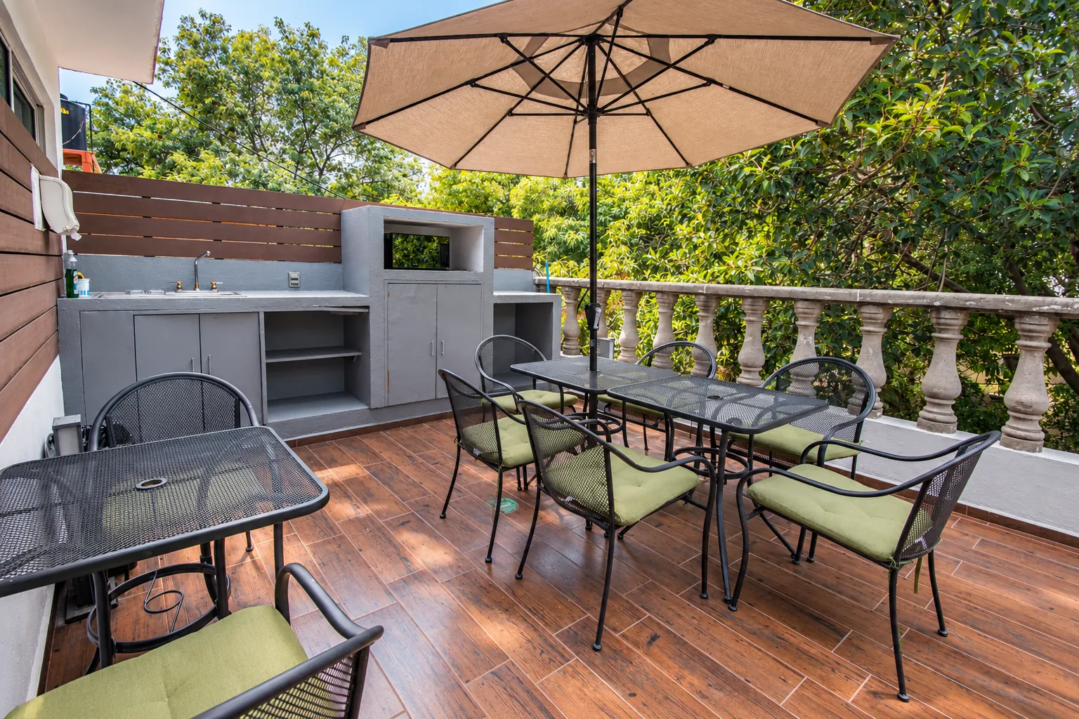 Terraza con sombrilla, mesas, sillas con cojines verdes y cocineta exterior, OfiRent Roma, Ciudad de México